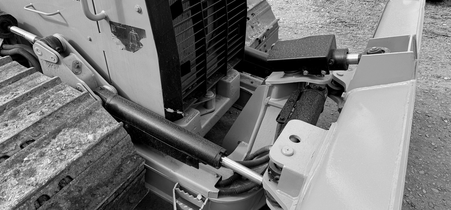 Hydraulic hoses and a cylinder rod at a dozer blade's pivot linkage, mounted between the track frame and blade back