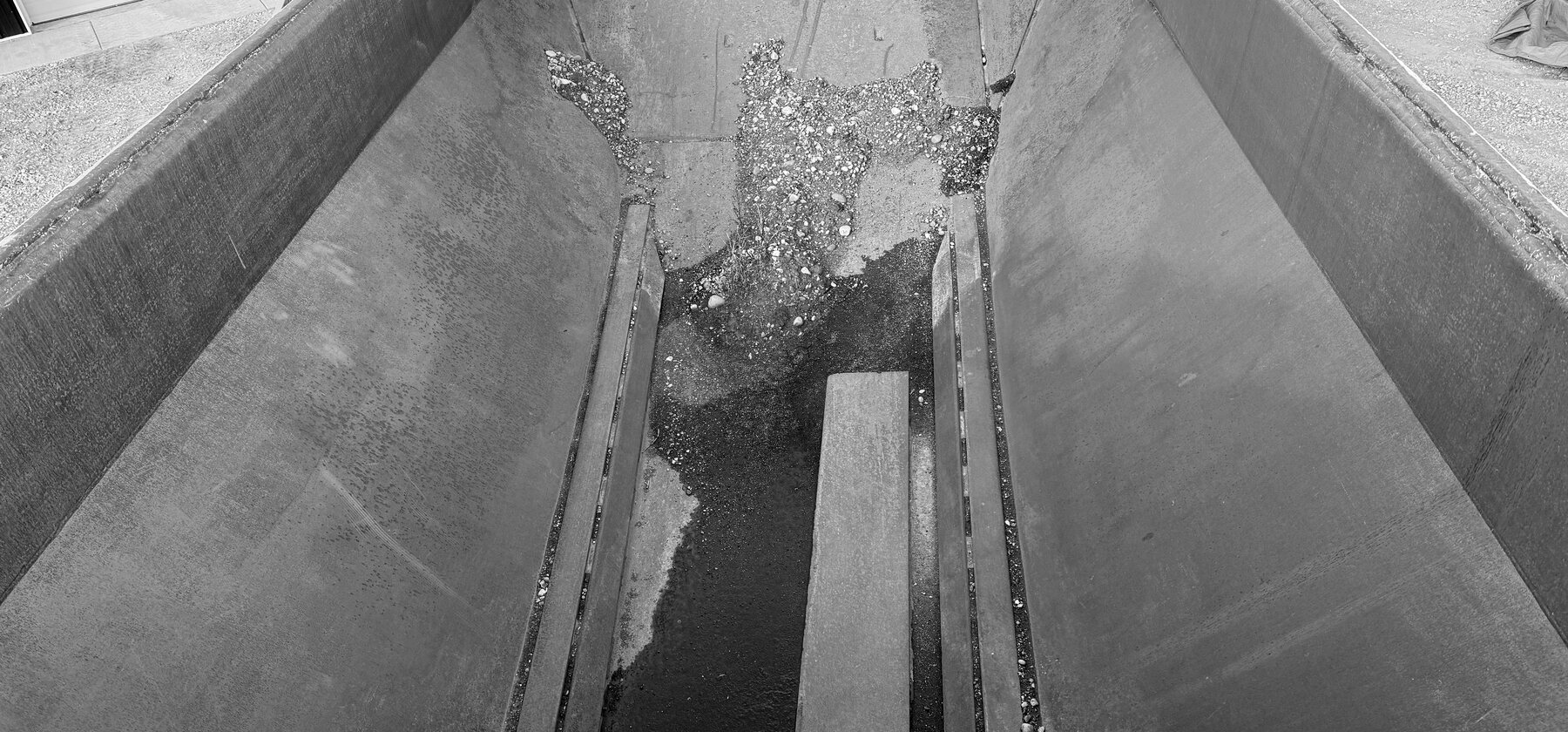 The inside of a rock truck dump box, worn steel converging toward the tailgate