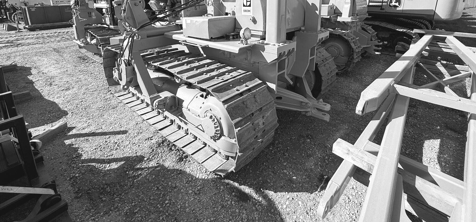A row of side boom pipelayers parked together in a yard, tracks and counterweight boxes lined up