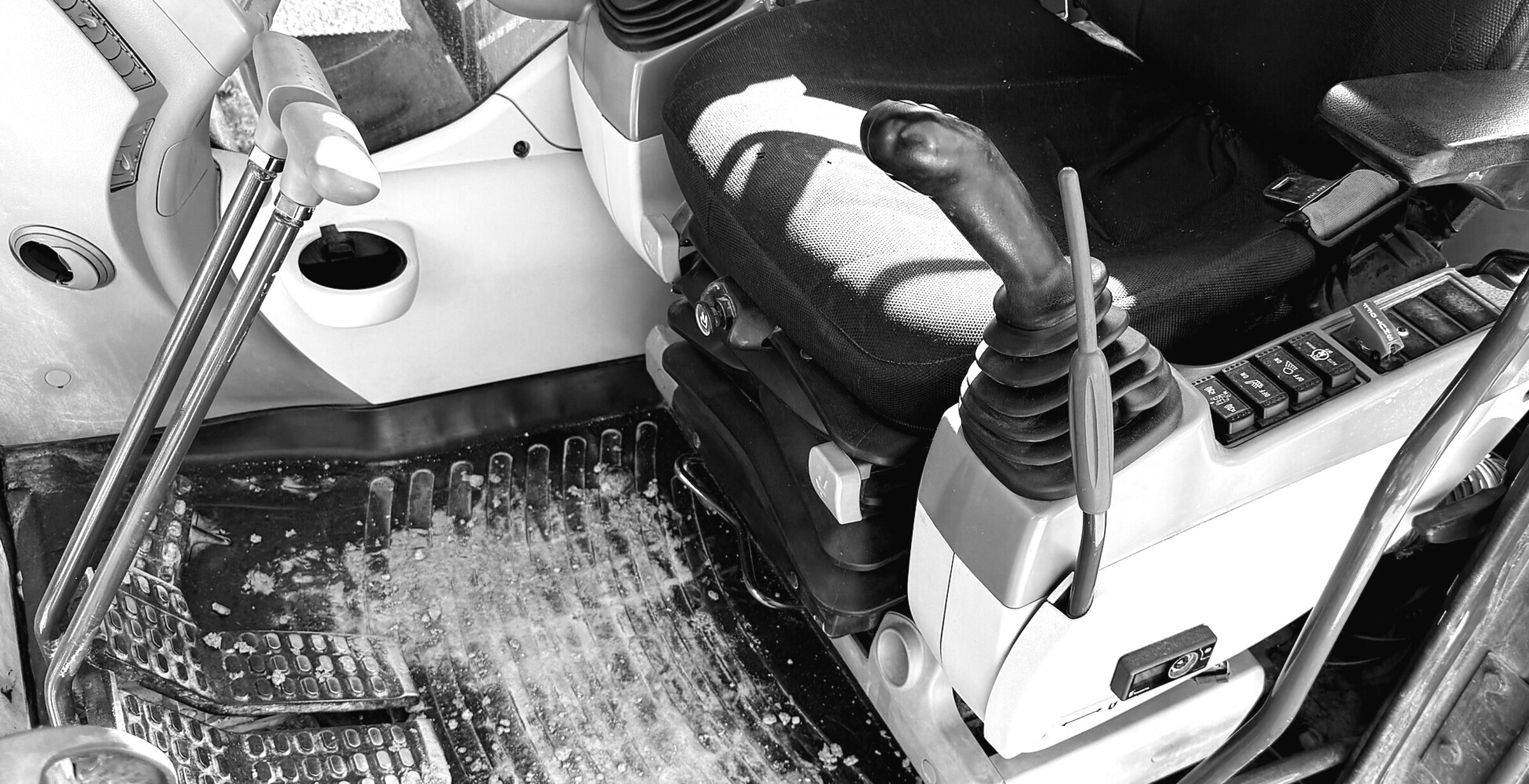 An excavator cab: the seat, both joysticks, the switch panel and the floor pedals