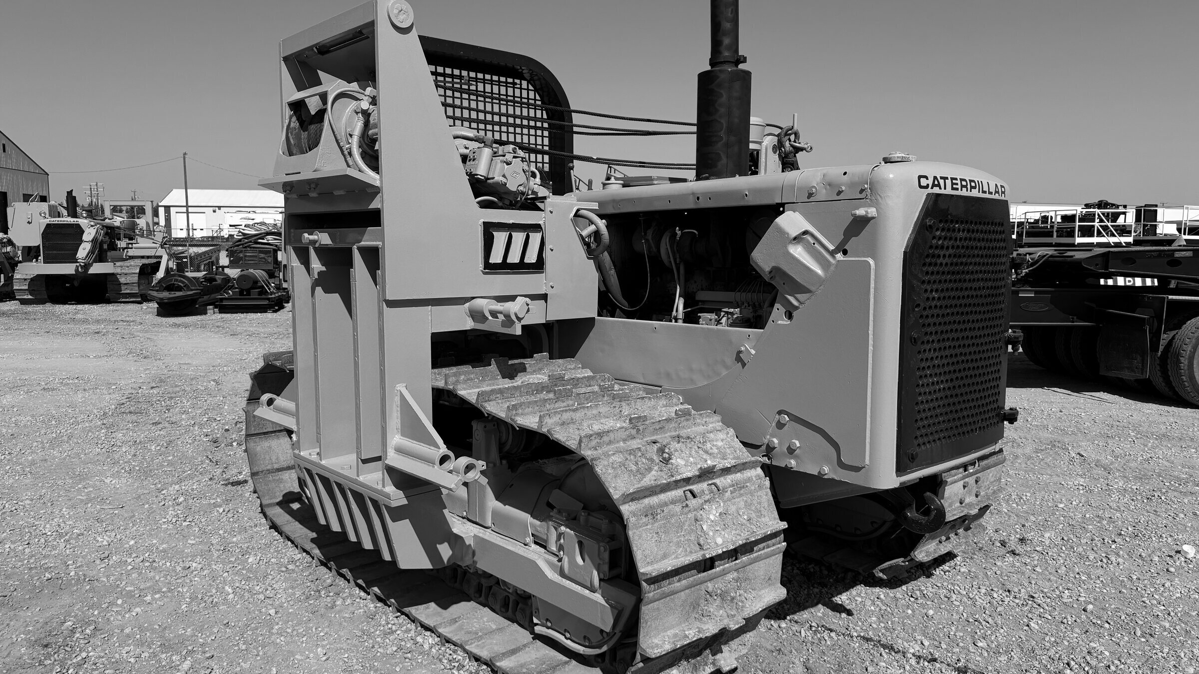 A tracked pipelayer standing in a yard, its boom folded over the hood