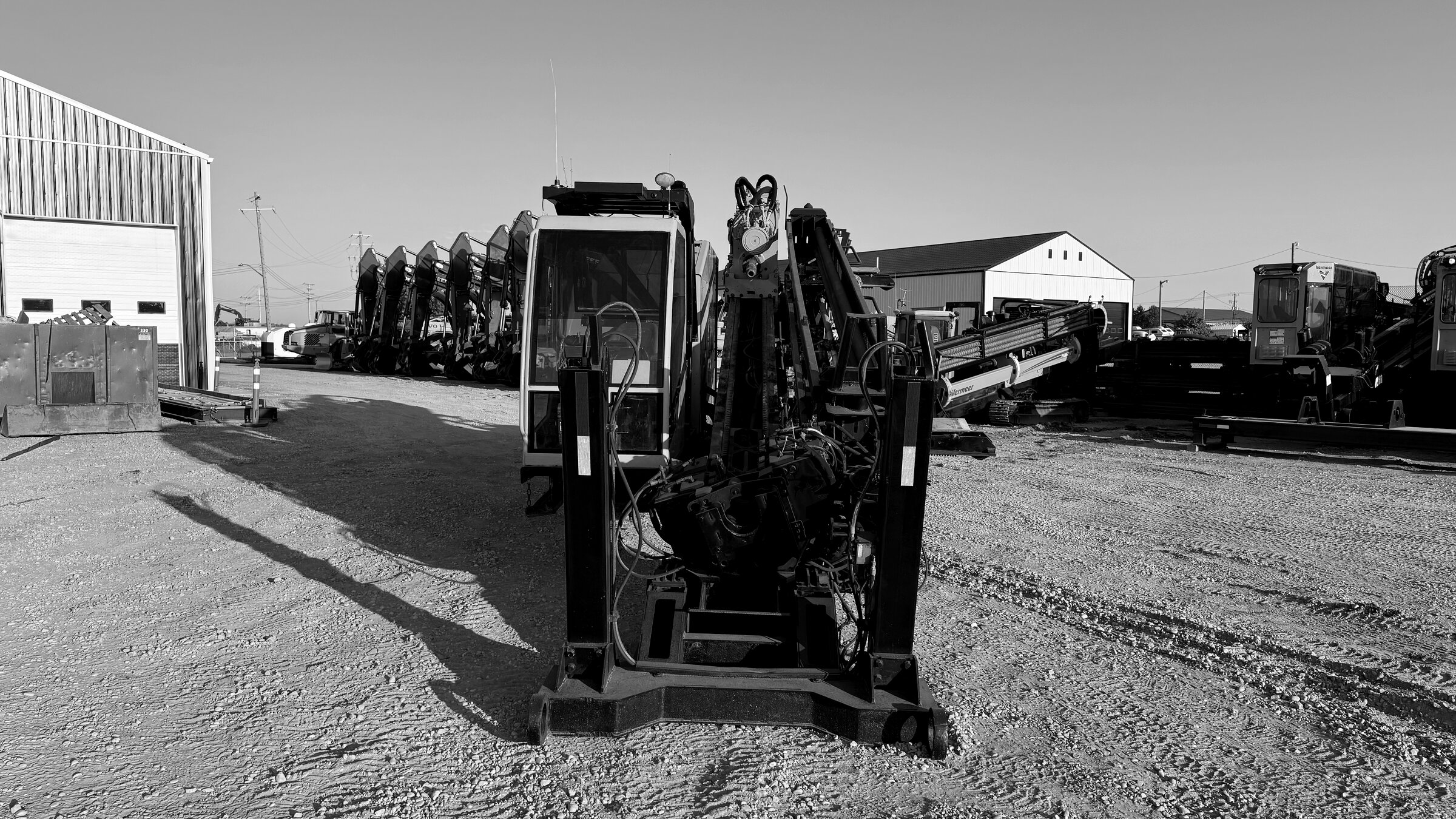 A tracked drill rig standing on a gravel pad, mast and carriage folded down