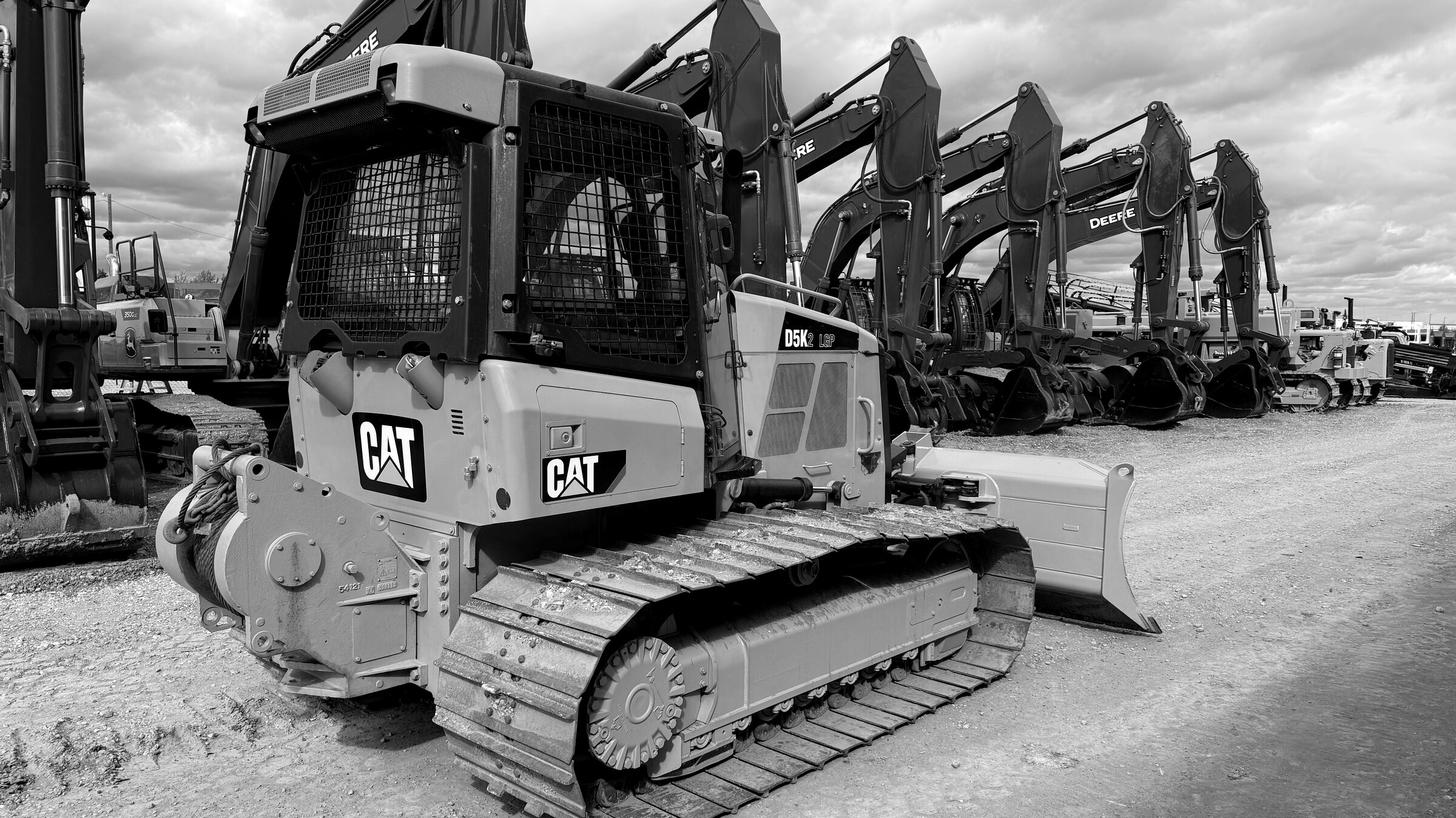 A line of tracked dozers and excavators standing nose-on in a yard