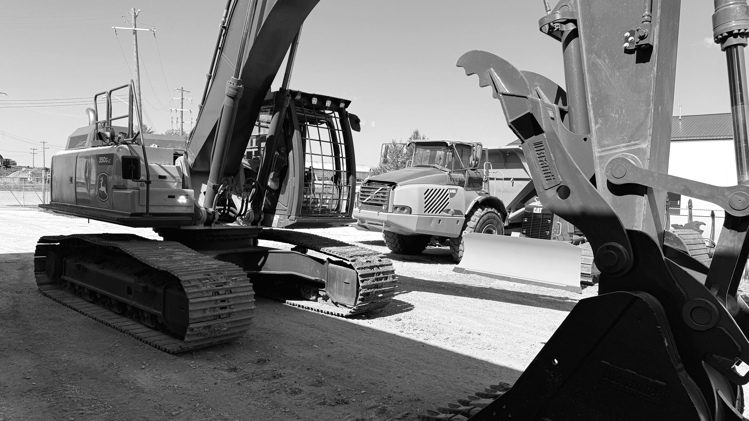 A tracked excavator in a yard, its boom and stick reaching across the frame