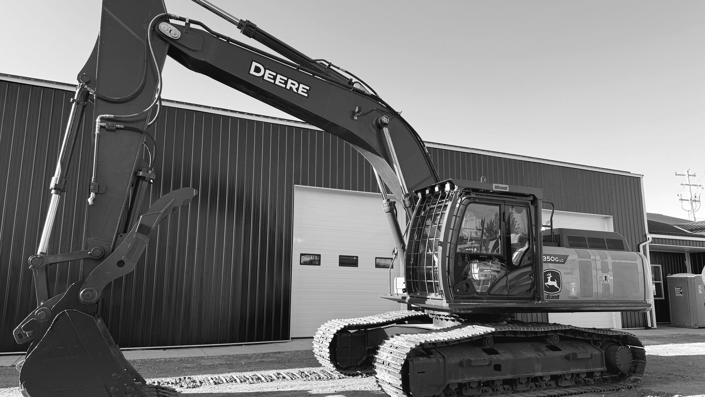 A tracked excavator with its bucket curled, standing against a shop wall