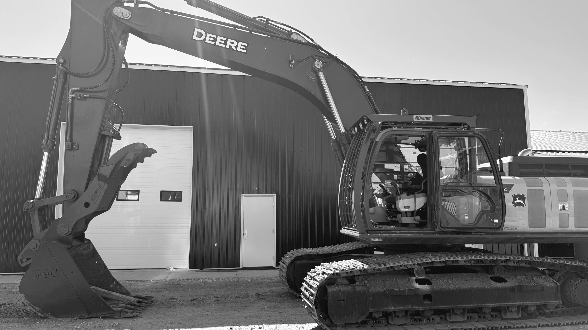 A tracked excavator standing alongside a shop, boom folded and bucket down