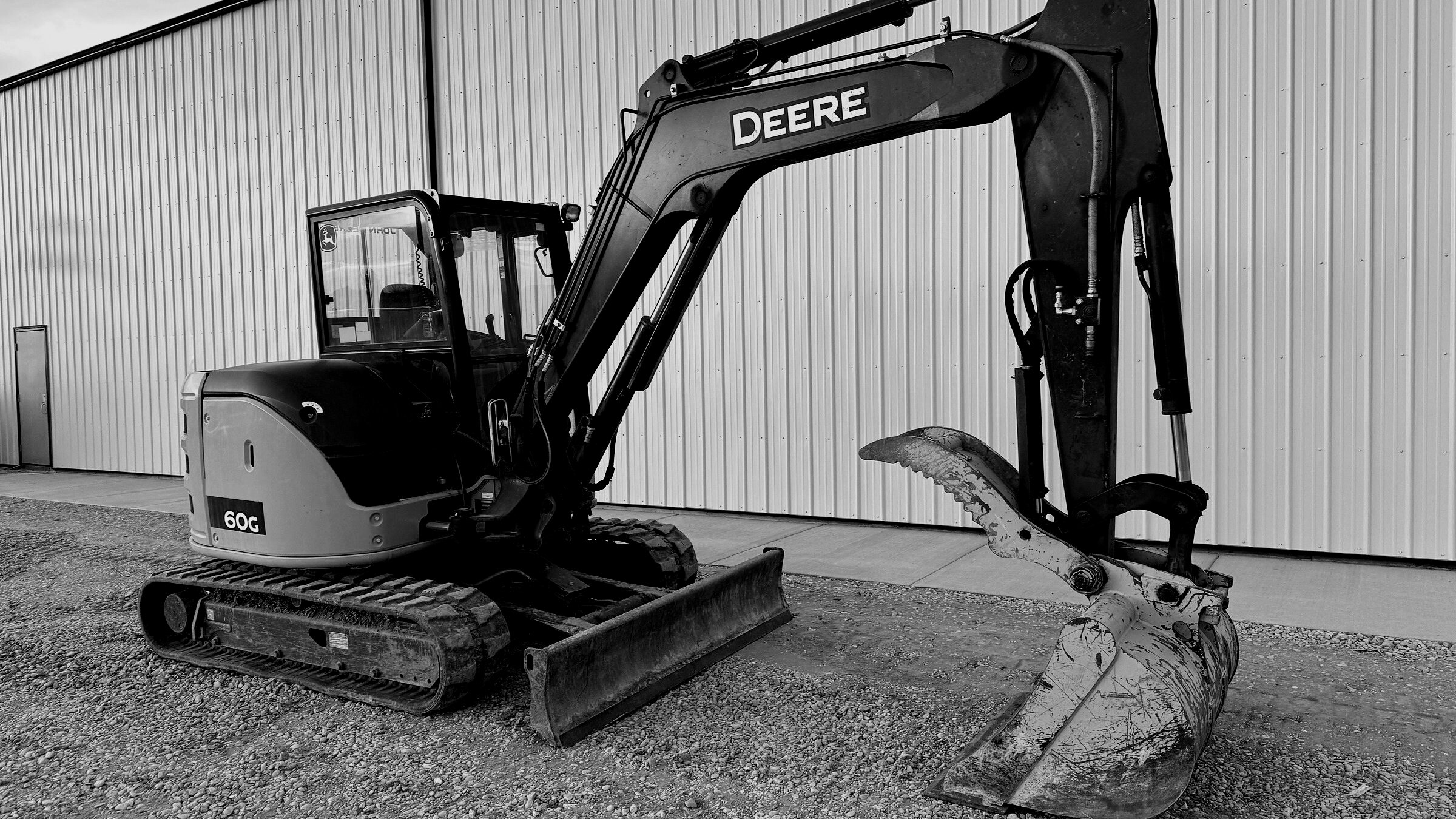 A mini excavator standing against a shop wall, bucket resting on the ground