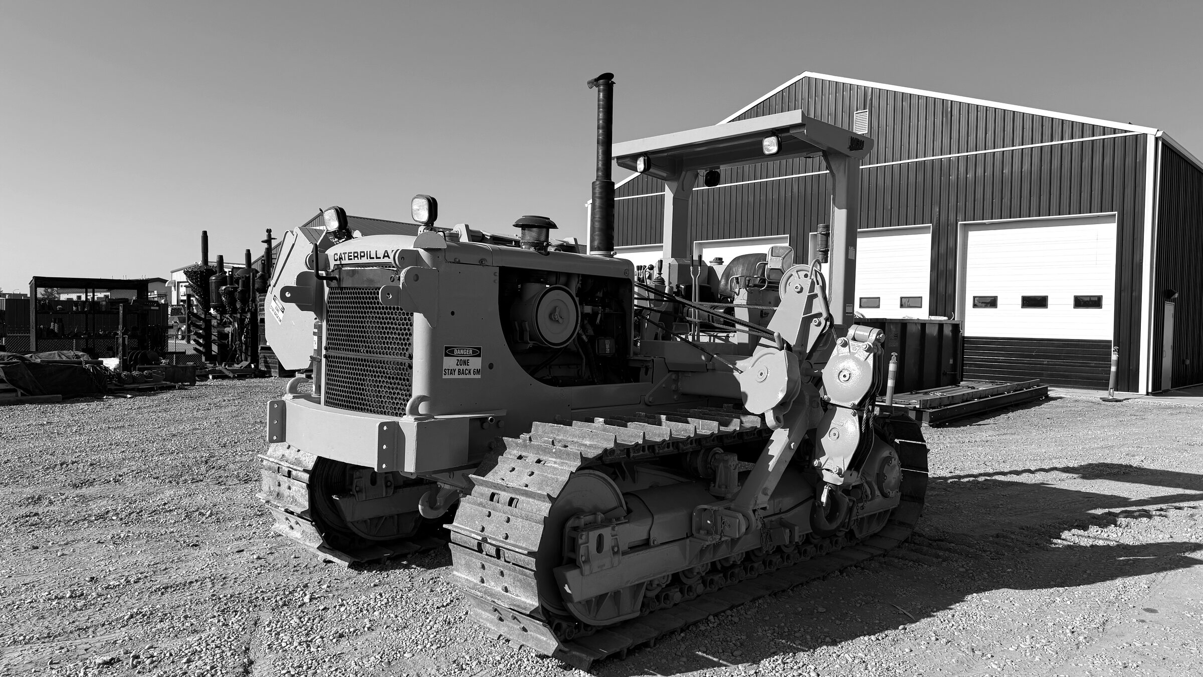 A tracked pipelayer standing outside a shop, its boom and winch stowed