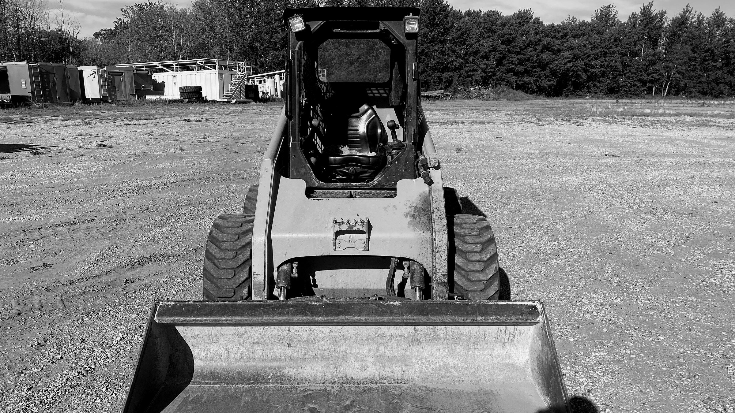 A tracked skid steer seen head-on, bucket down on the gravel