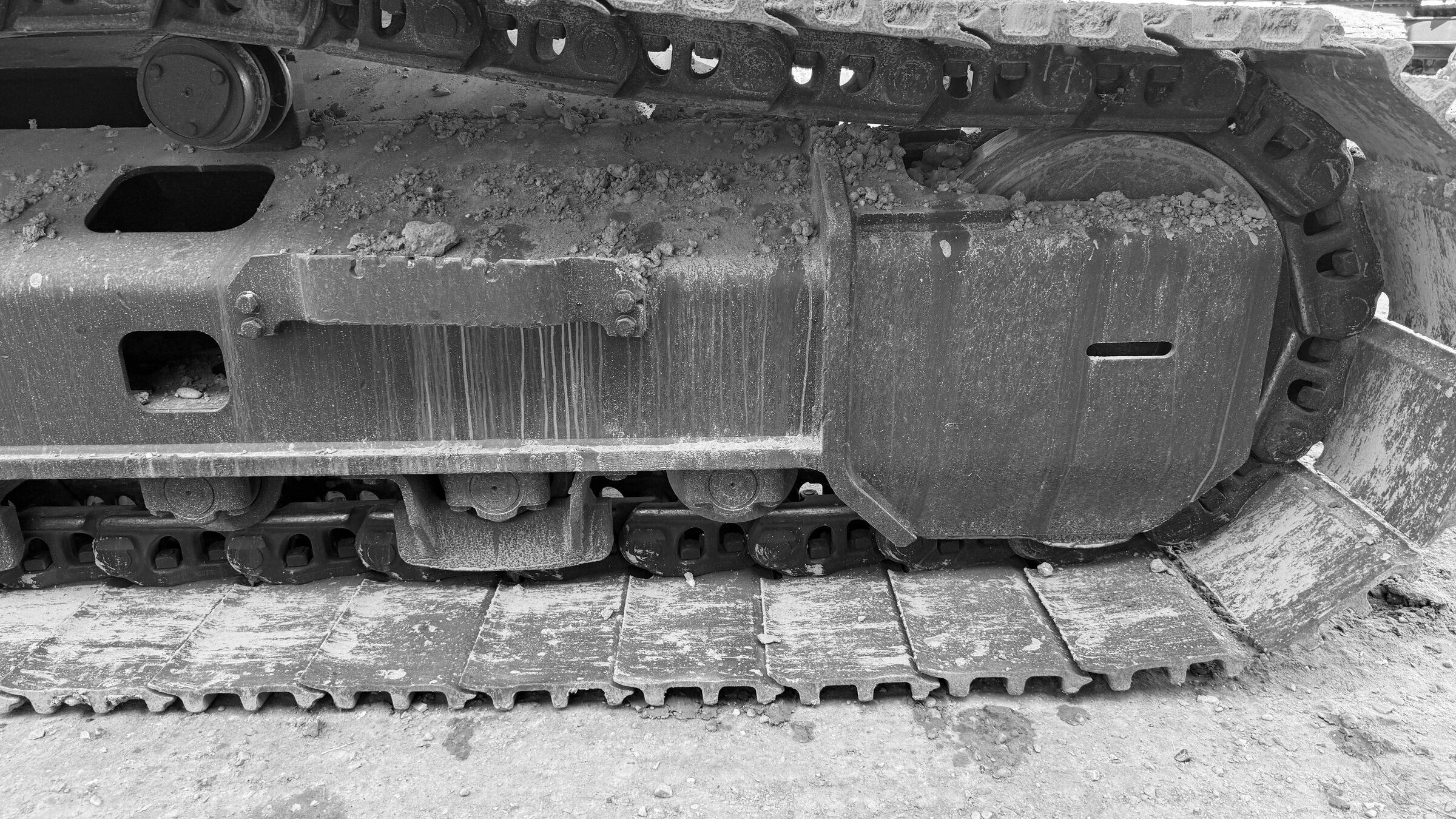 A track frame and idler on an excavator, the chain and pads packed with dried ground
