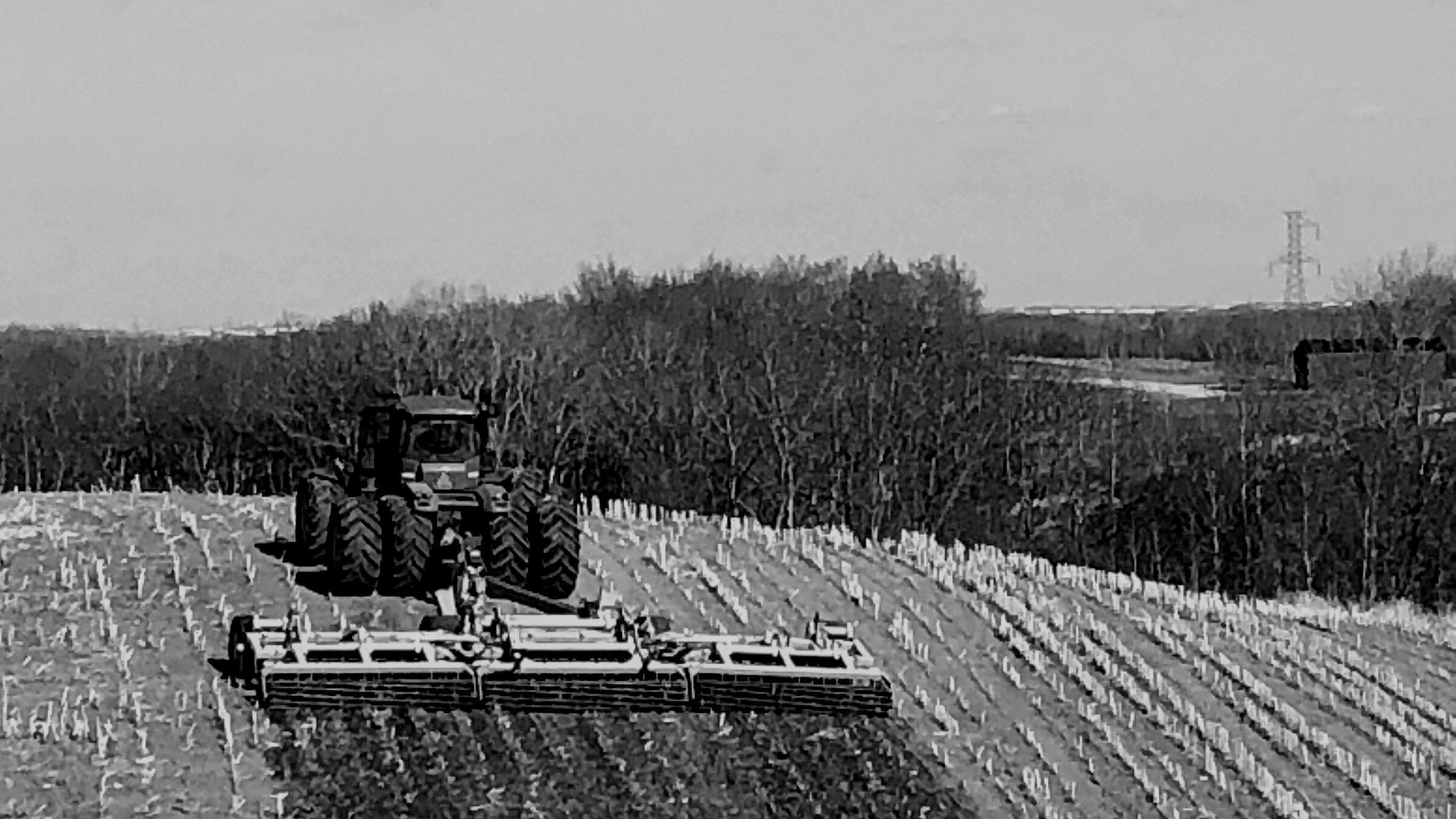 A tractor pulling a disc across a field, working away from the camera
